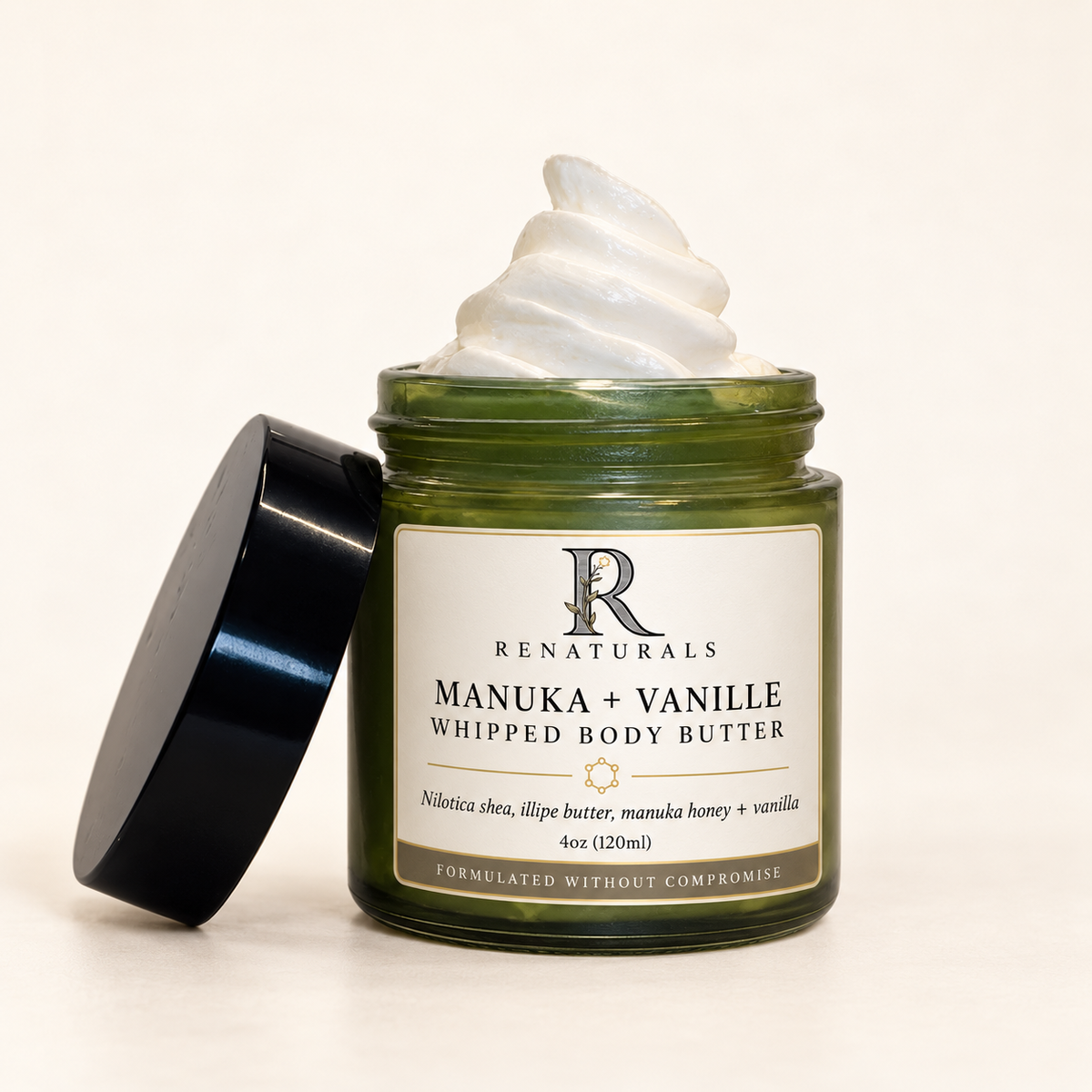 RENATURALS Manuka + Vanille Whipped Body Butter, 4oz, showing its whipped cream texture in an open green glass jar with the black lid beside it and a gold-trim Botanical R label on ivory.